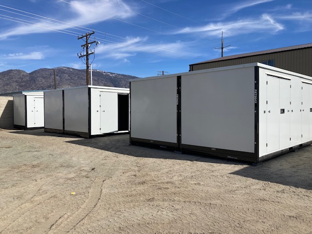 Two large white industrial containers parked on a dirt lot under a blue sky.