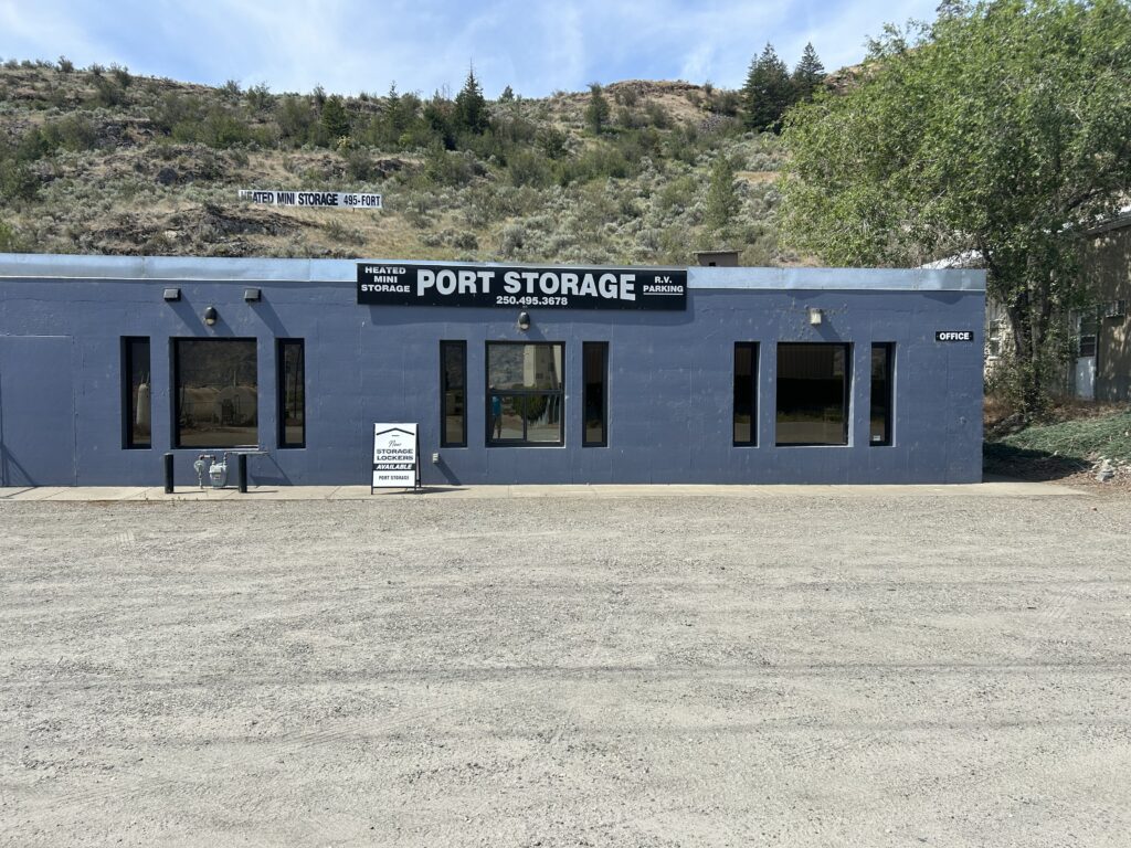 A blue building labeled 'Port Storage' with a gravel foreground and trees behind.