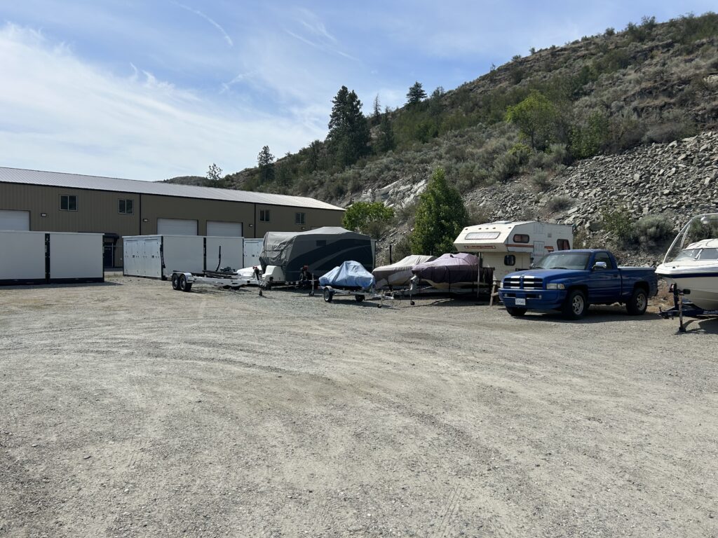 Vehicles and trailers parked beside a warehouse near a hillside.